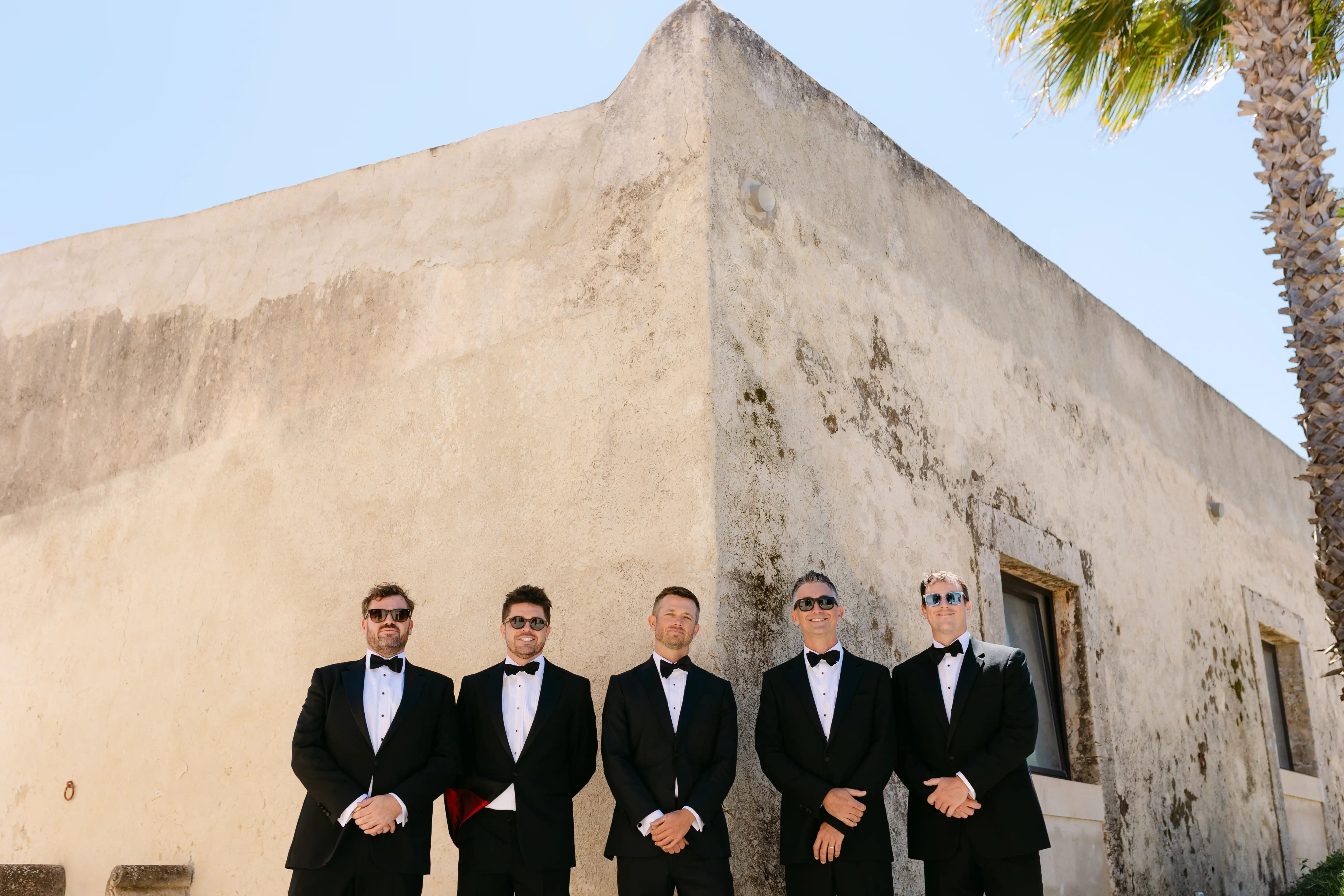 Groom and groomsmen portrait in tuxedos outside a historic Sicilian wedding venue